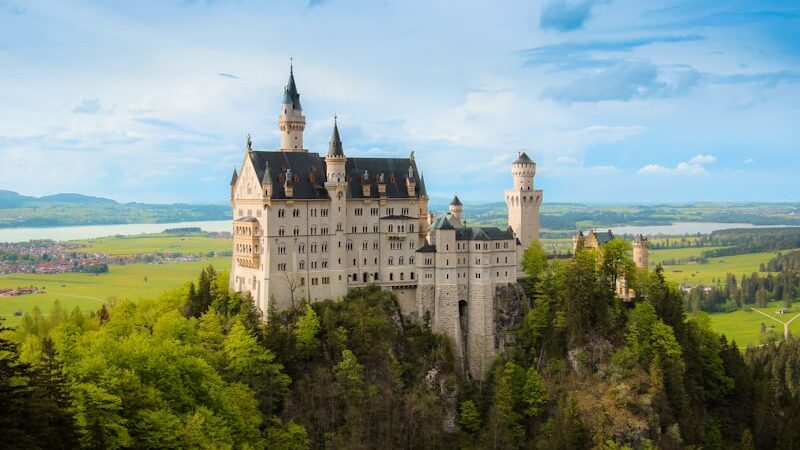 **"Neuschwanstein Castle in Bavaria, Germany, surrounded by lush green hills and blue sky, resembling a fairytale palace."**
